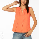 Woman wearing coral sleeveless top with tie neck detail and jeans