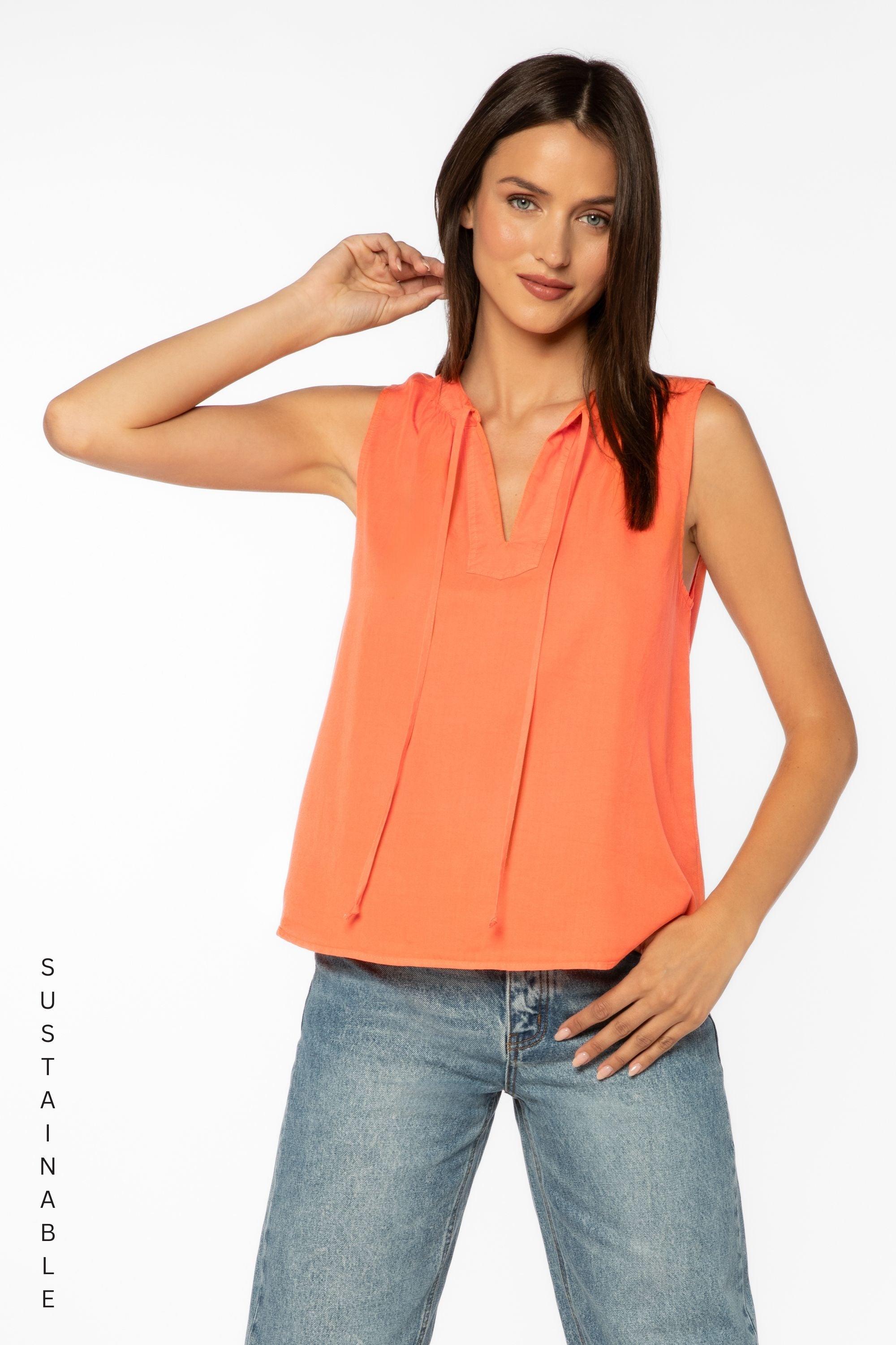 Woman wearing coral sleeveless top with tie neck detail and jeans
