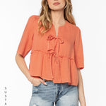 Woman wearing coral Bevie top with tie details and denim shorts