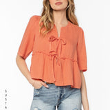 Woman wearing coral Bevie top with tie details and denim shorts