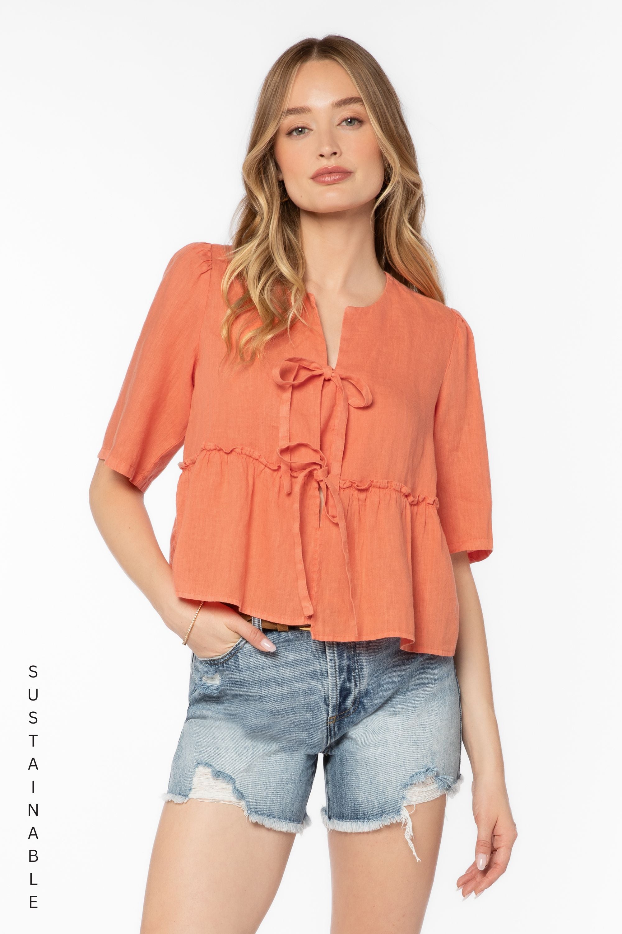 Woman wearing coral Bevie top with tie details and denim shorts