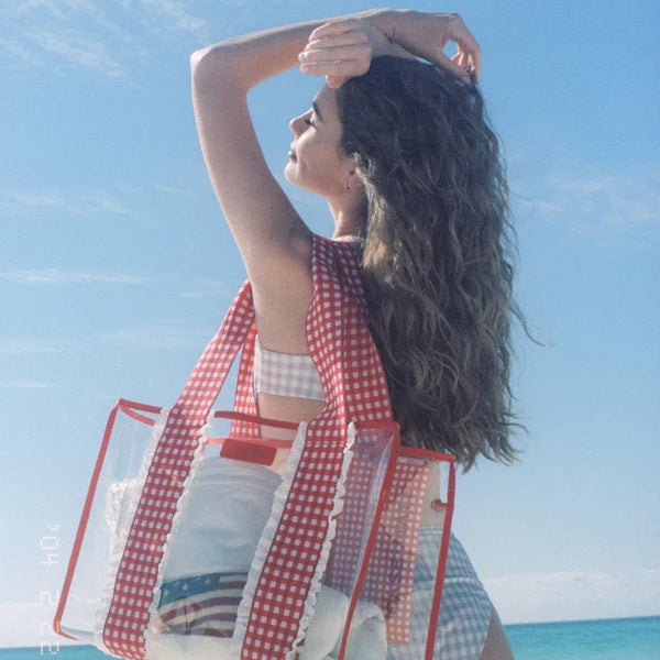 Woman holding clear gingham tote bag with red checkered pattern against blue sky