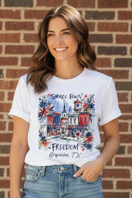 Woman wearing white Small Town Freedom Grapevine TX watercolor patriotic t-shirt at ooh la la! in Grapevine TX 76051
