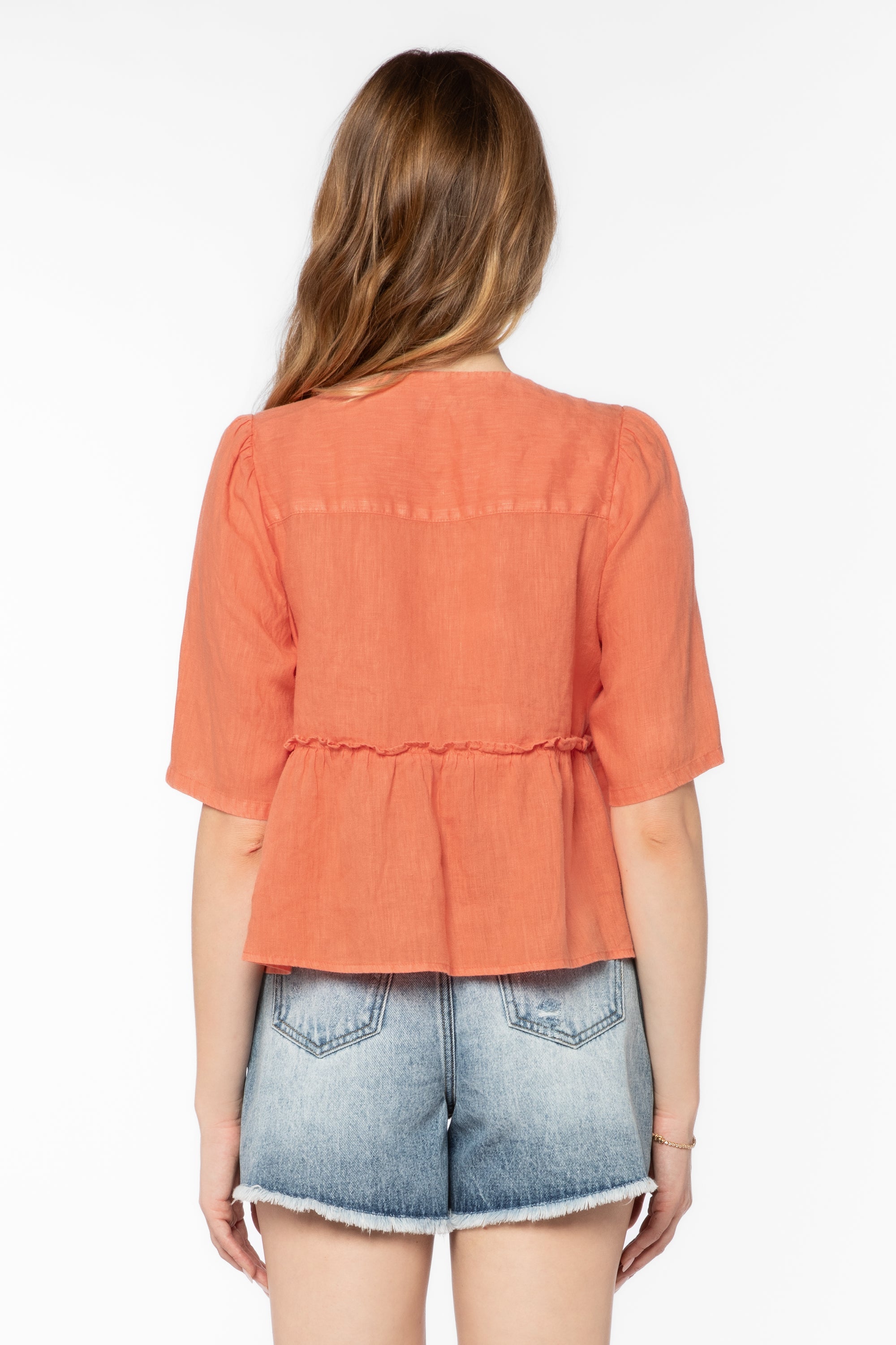 Back view of woman wearing coral orange Bevie top with denim shorts