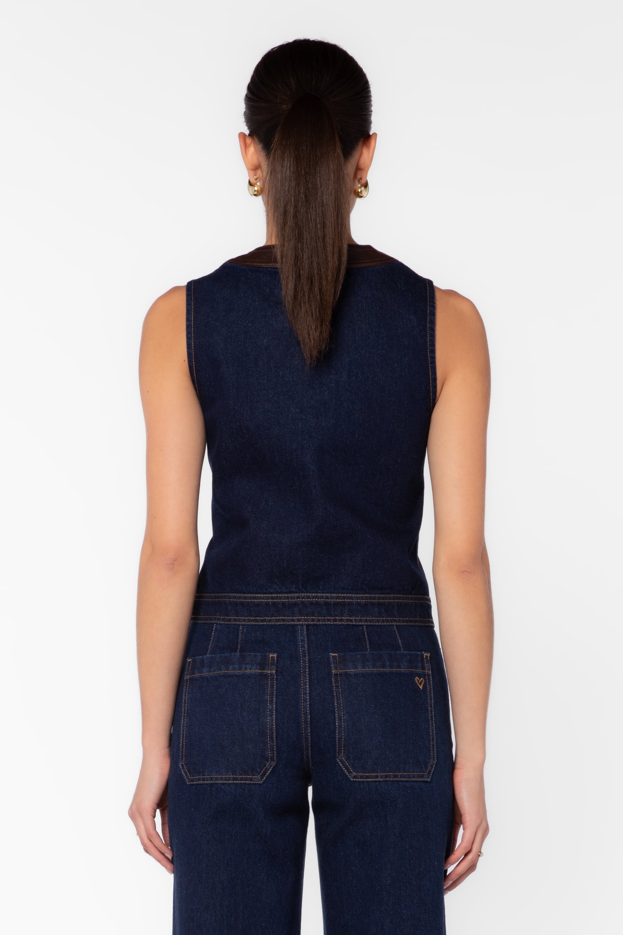 Back view of dark navy denim vest with brown leather trim and matching wide-leg jeans