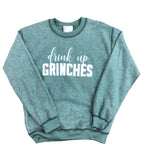 Washed sage green crewneck sweatshirt featuring the white graphic text "drink up" in a script font above the bold block text "GRINCHES." The sweatshirt has a faded, pigment-dyed finish.