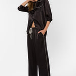 Woman wearing black satin wide-leg pants with white piping trim and matching shirt