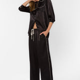 Woman wearing black satin wide-leg pants with white piping trim and matching shirt
