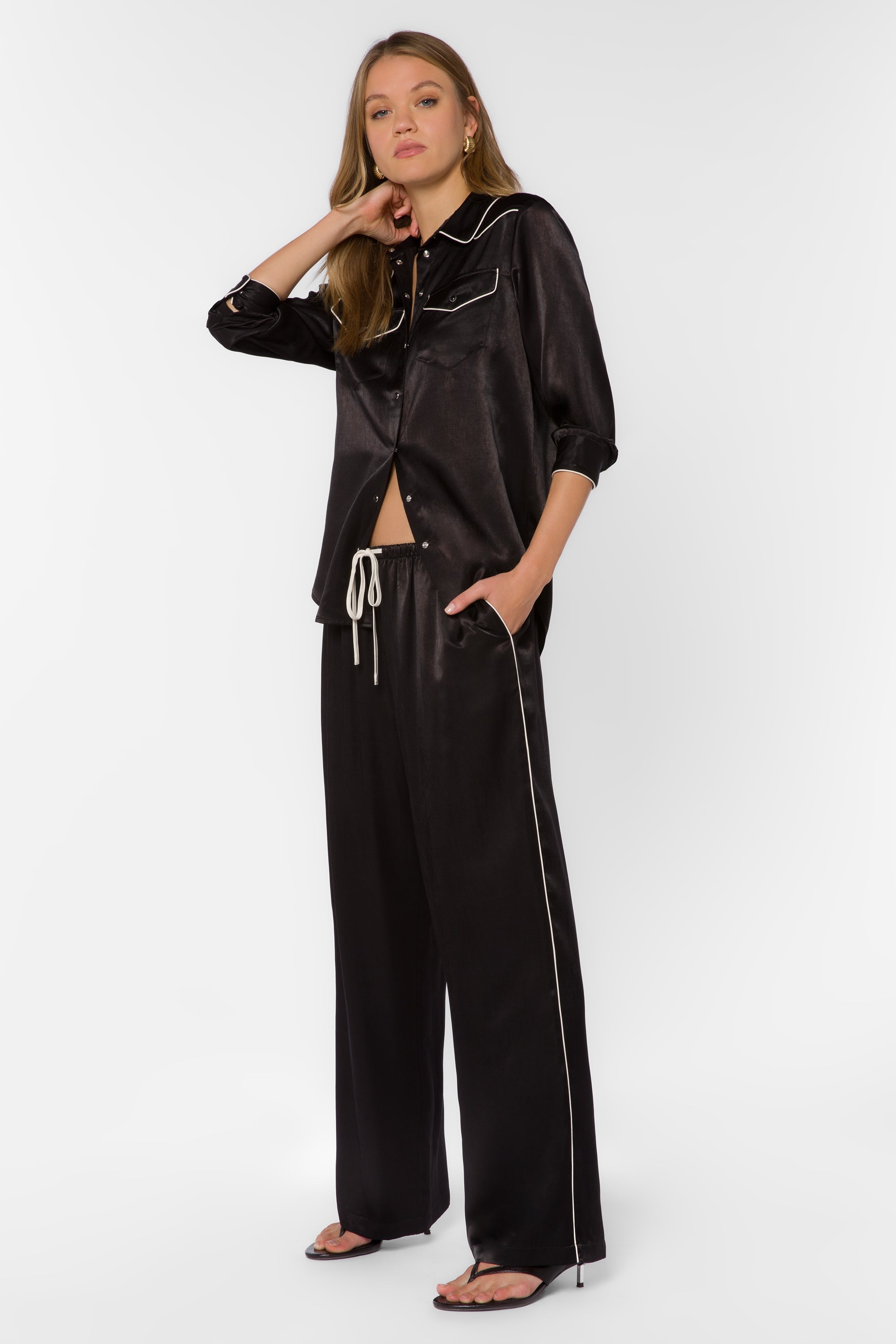 Woman wearing black satin wide-leg pants with white piping trim and matching shirt