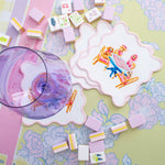 Taylor Paladino Dogs Playing Mahjong cocktail squares with scalloped pink border styled with mahjong tiles and purple glass