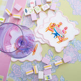 Taylor Paladino Dogs Playing Mahjong cocktail squares with scalloped pink border styled with mahjong tiles and purple glass