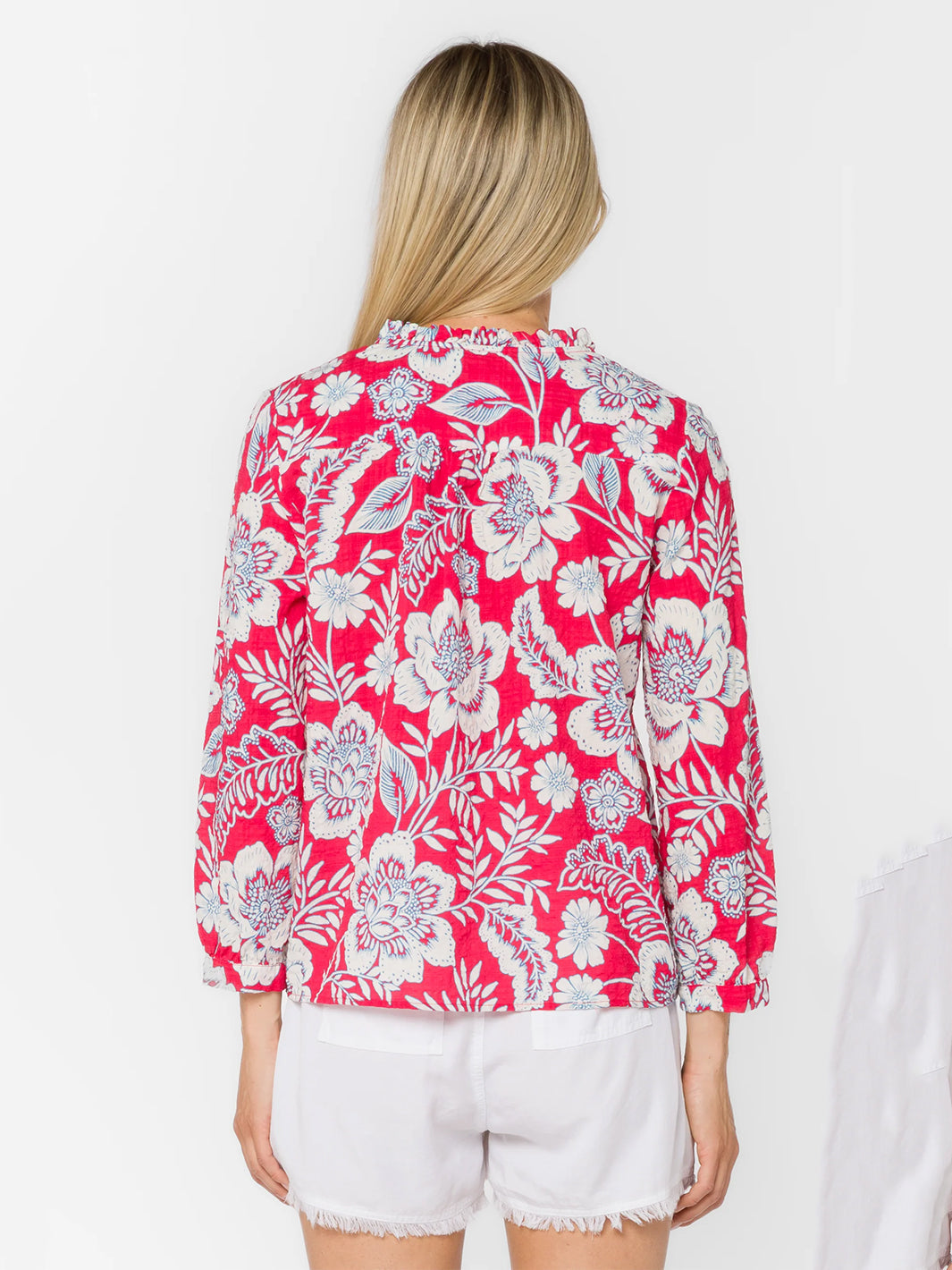 Woman wearing pink floral blouse with white shorts, back view studio shot