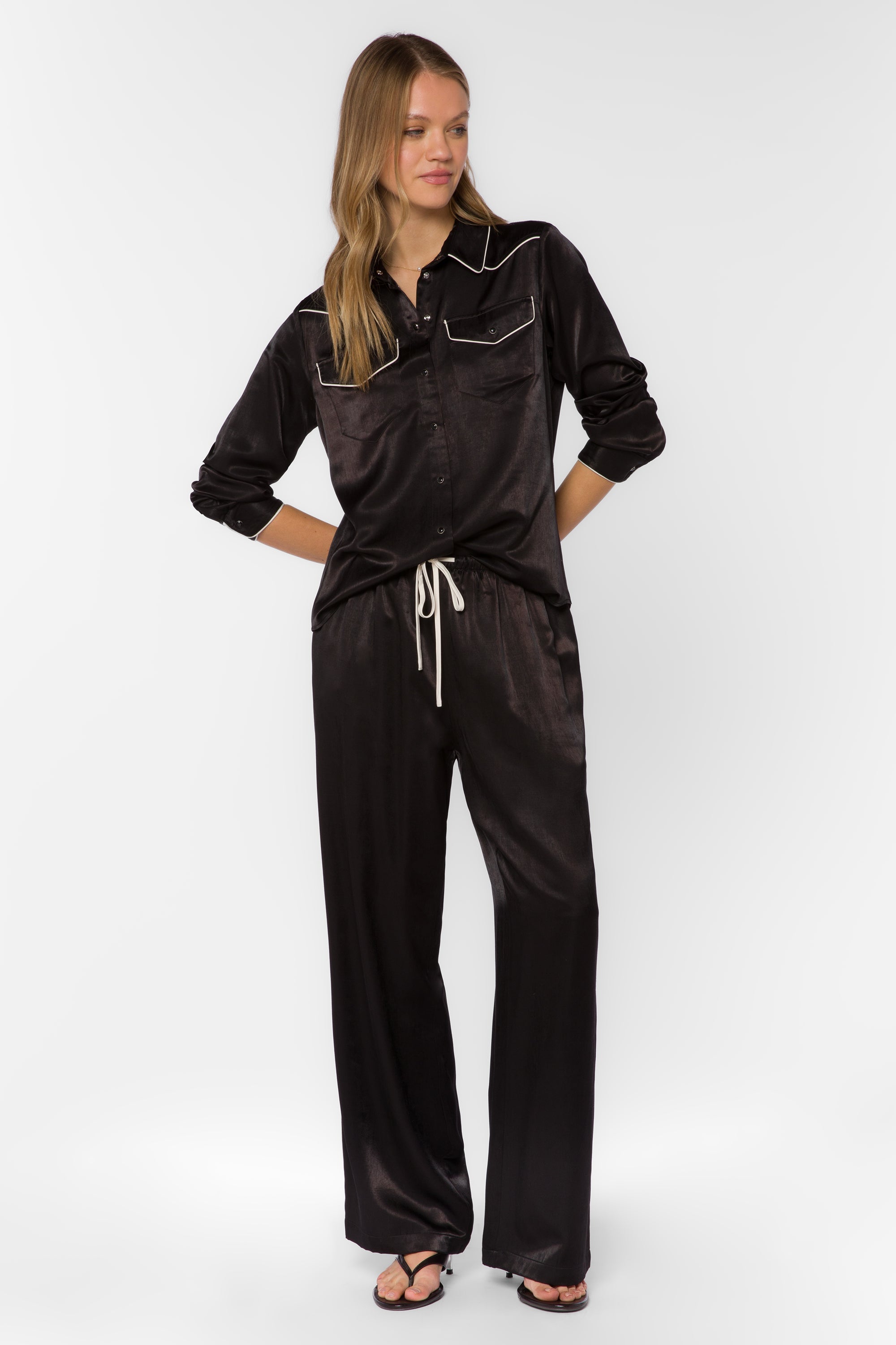 Woman wearing black satin western-style shirt with cream contrast trim and matching pants