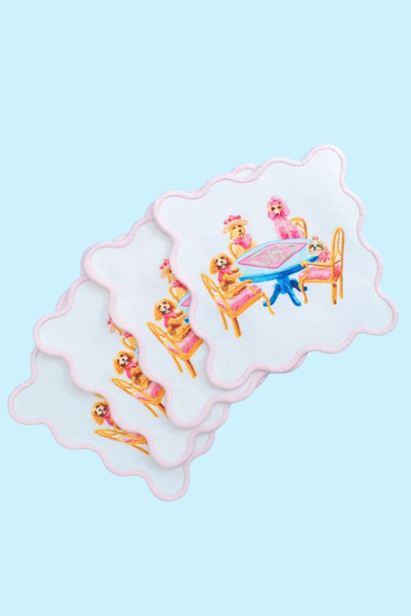 Set of four white scalloped cocktail napkins printed with poodles playing mahjong at a blue table