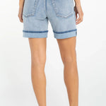Woman wearing light blue denim cuffed shorts with rolled hems, back view