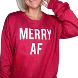 Close-up of a smiling woman wearing a bright red heathered crewneck sweatshirt with the bold white text "MERRY AF" printed across the front.
