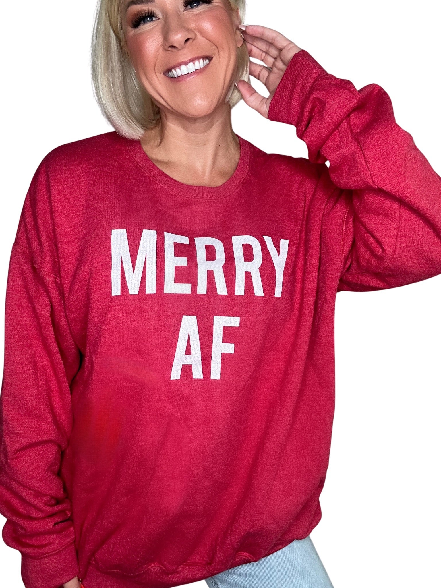 Close-up of a smiling woman wearing a bright red heathered crewneck sweatshirt with the bold white text "MERRY AF" printed across the front.