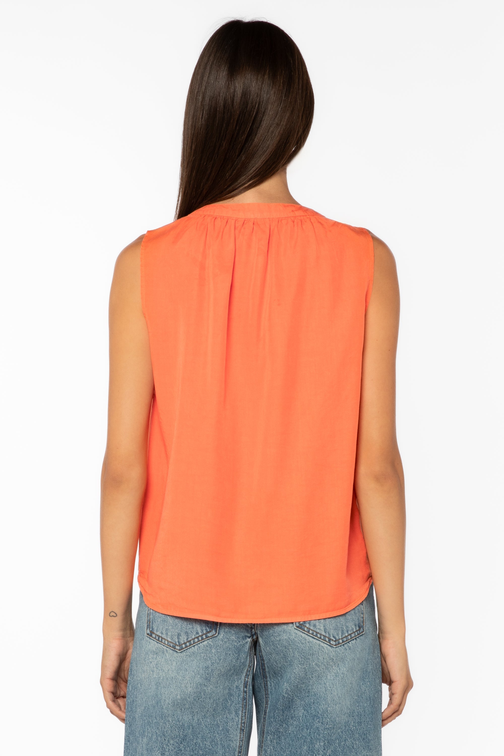 Back view of woman wearing coral sleeveless top with jeans