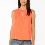 Woman wearing coral sleeveless top with tie neck detail and blue jeans