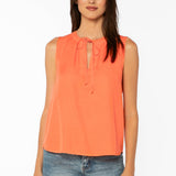 Woman wearing coral sleeveless top with tie neck detail and blue jeans
