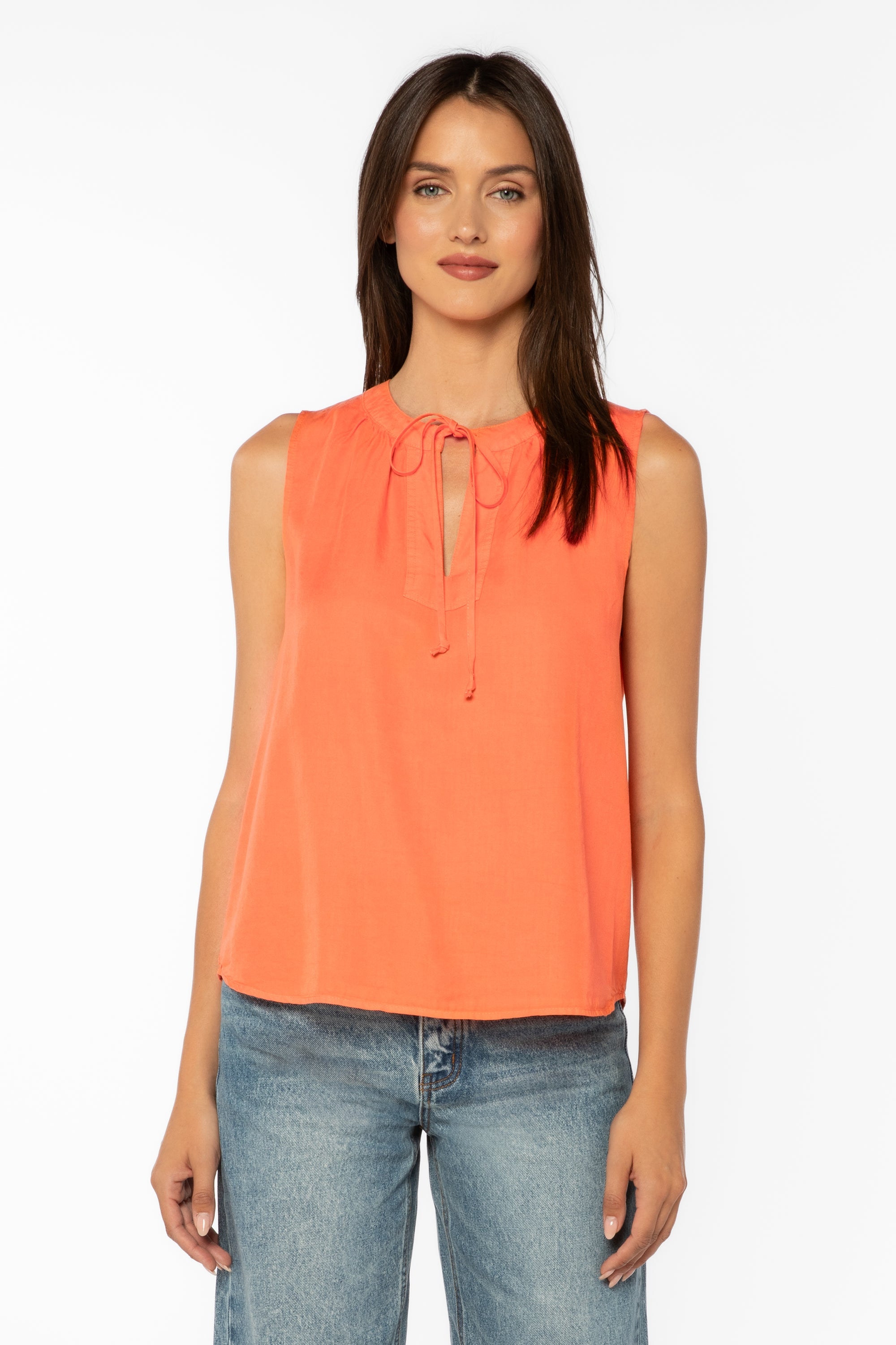 Woman wearing coral sleeveless top with tie neck detail and blue jeans