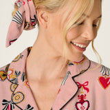 Smiling blonde woman wearing PJ Salvage Love Lockets pink flannel pajama top with matching scrunchie