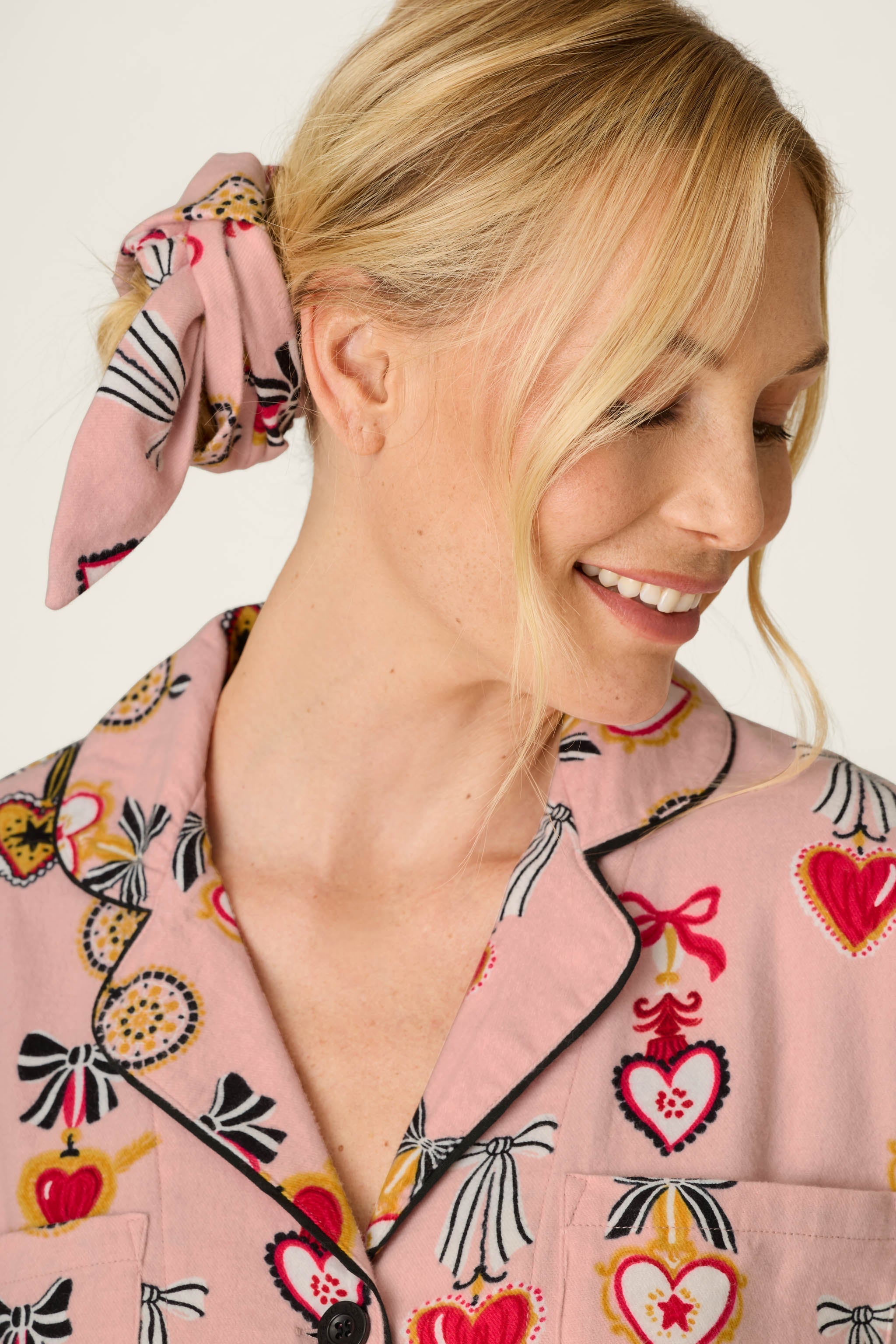 Smiling blonde woman wearing PJ Salvage Love Lockets pink flannel pajama top with matching scrunchie