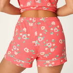 Woman wearing coral floral print pajama shorts and matching crop top set