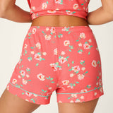 Woman wearing coral floral print pajama shorts and matching crop top set