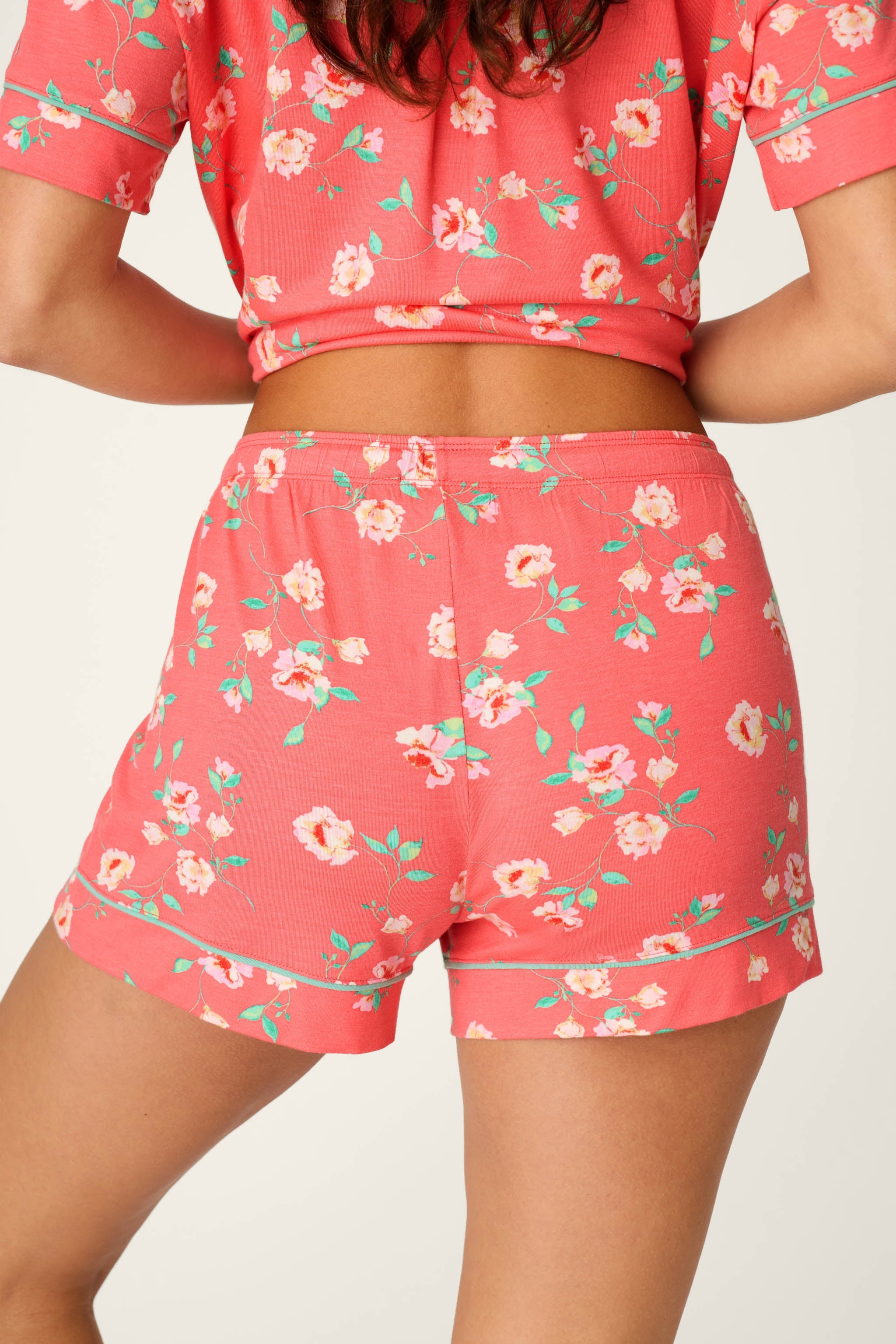 Woman wearing coral floral print pajama shorts and matching crop top set