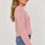 Woman wearing a fluffy soft pink eyelash knit sweater with blue jeans, side view.