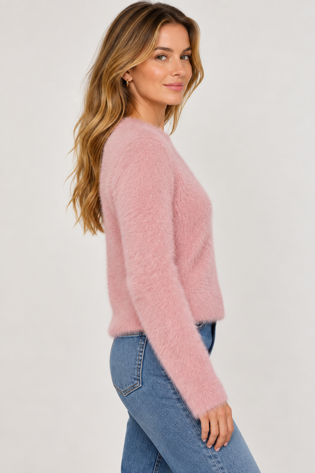 Woman wearing a fluffy soft pink eyelash knit sweater with blue jeans, side view.
