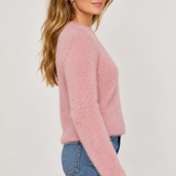 Woman wearing a fluffy soft pink eyelash knit sweater with blue jeans, side view.