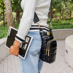 Woman carrying black shiny Wanderfull HydroBag with gold hardware crossbody while holding notebook