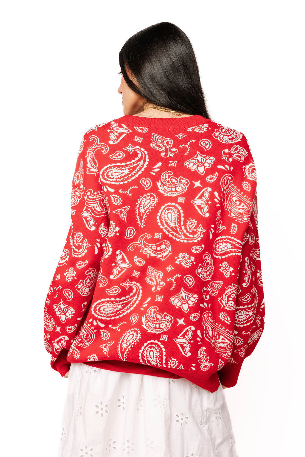 Back view of red and white paisley print knit sweater on female model with white skirt