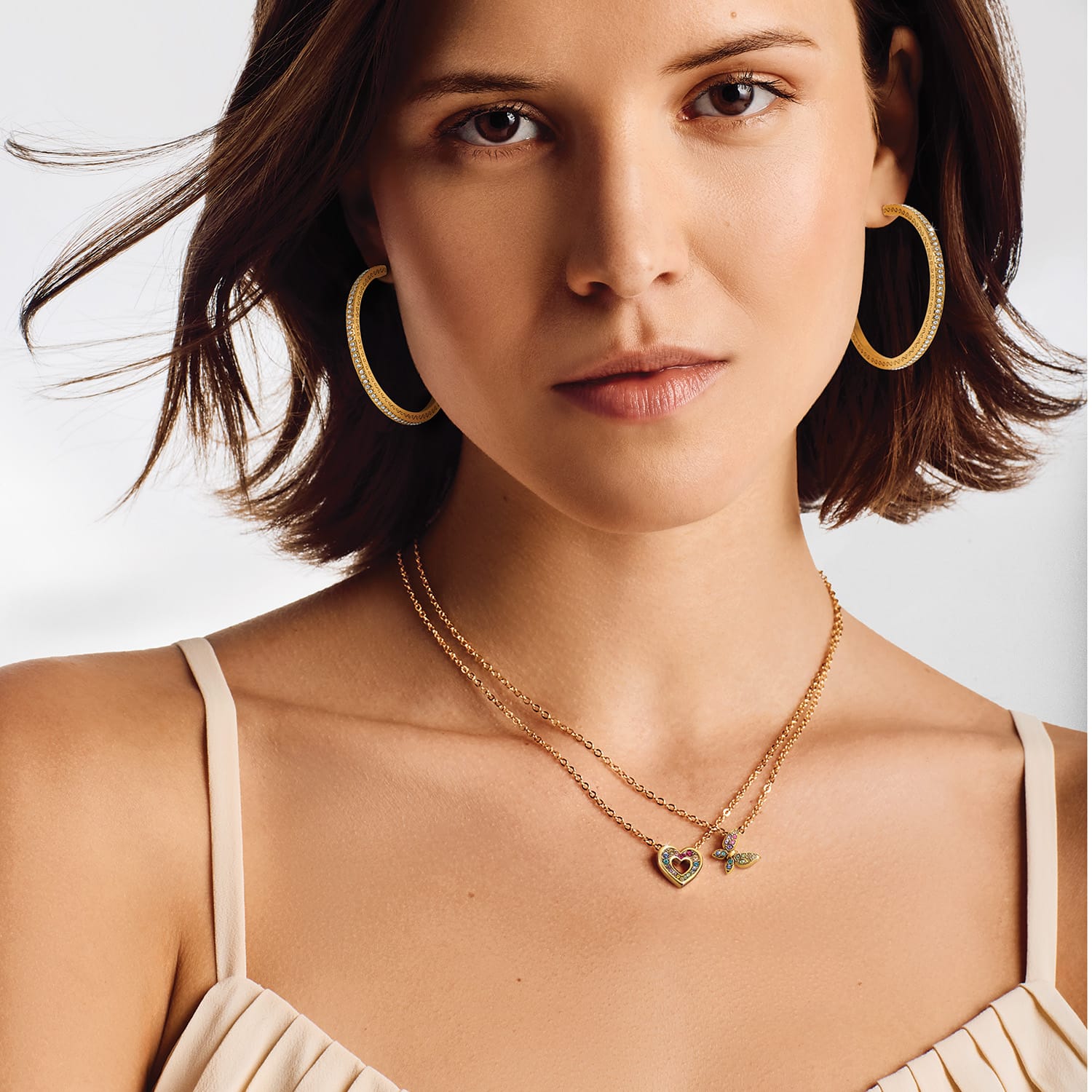 Woman wearing gold layered necklaces with heart and hummingbird charms featuring colorful gems