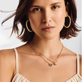 Woman wearing gold layered necklaces with heart and hummingbird charms featuring colorful gems
