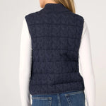 Woman wearing navy cable-knit quilted sweater vest over white long-sleeve top, back view