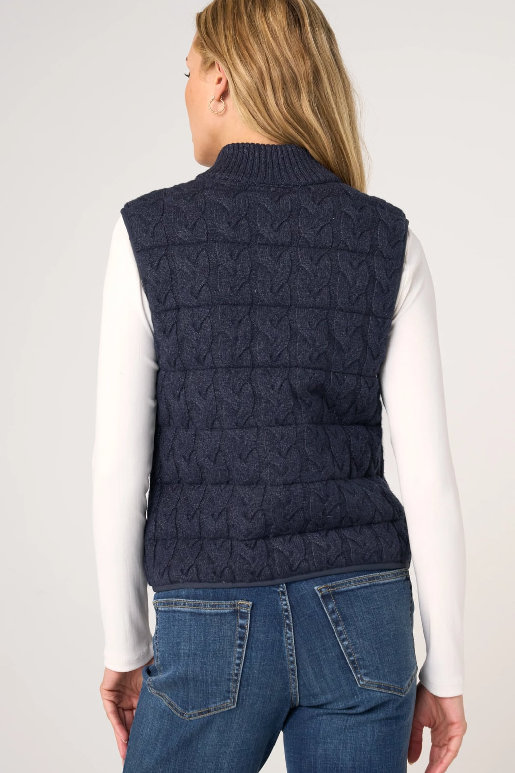 Woman wearing navy cable-knit quilted sweater vest over white long-sleeve top, back view