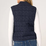 Woman wearing navy cable-knit quilted sweater vest over white long-sleeve top, back view