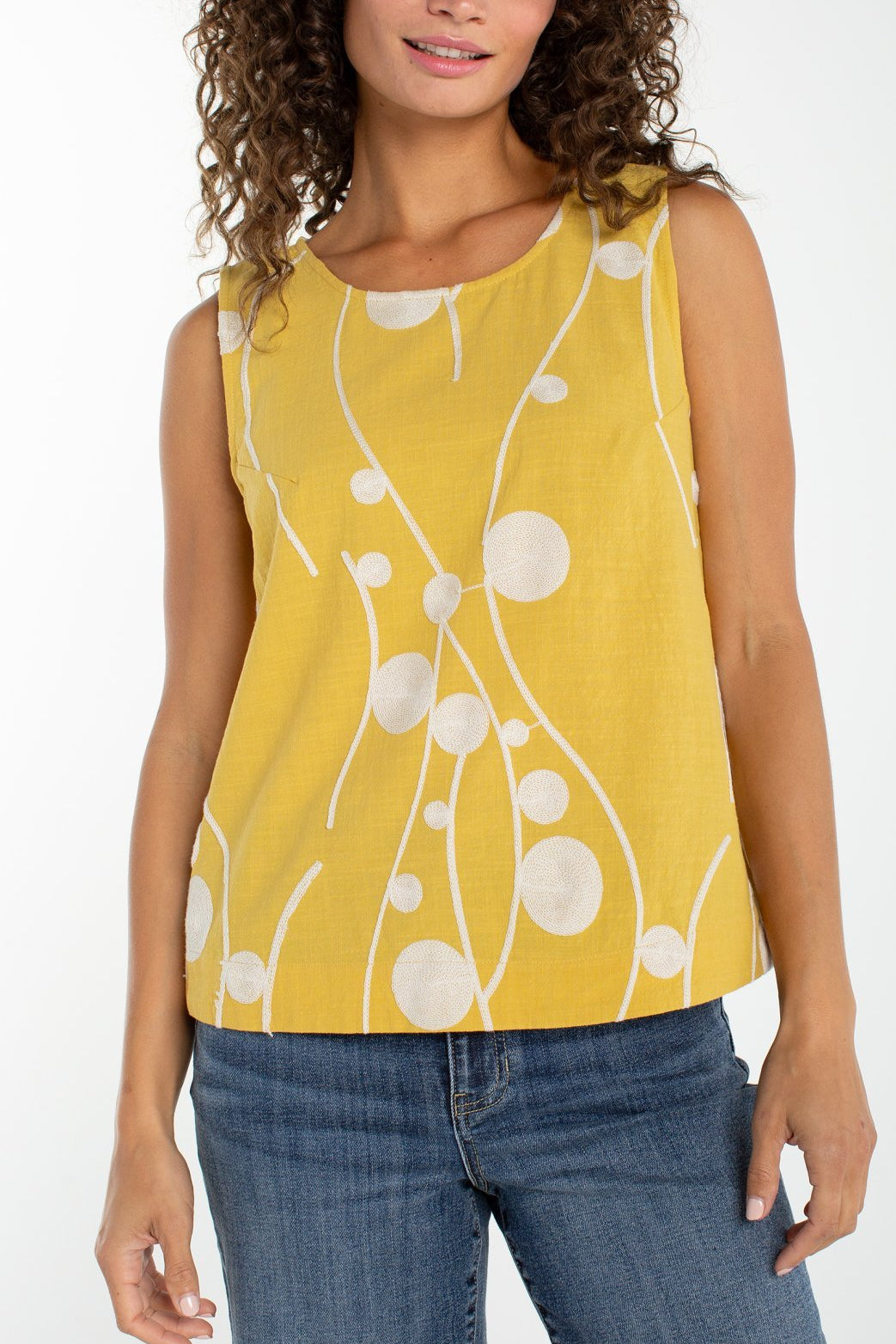 Woman wearing yellow sleeveless top with cream embroidered circles and curved lines