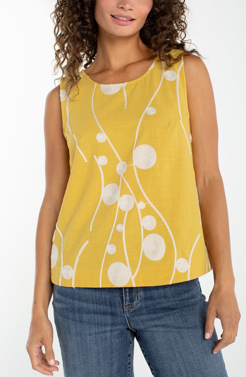 Woman wearing yellow sleeveless top with cream embroidered circles and curved lines