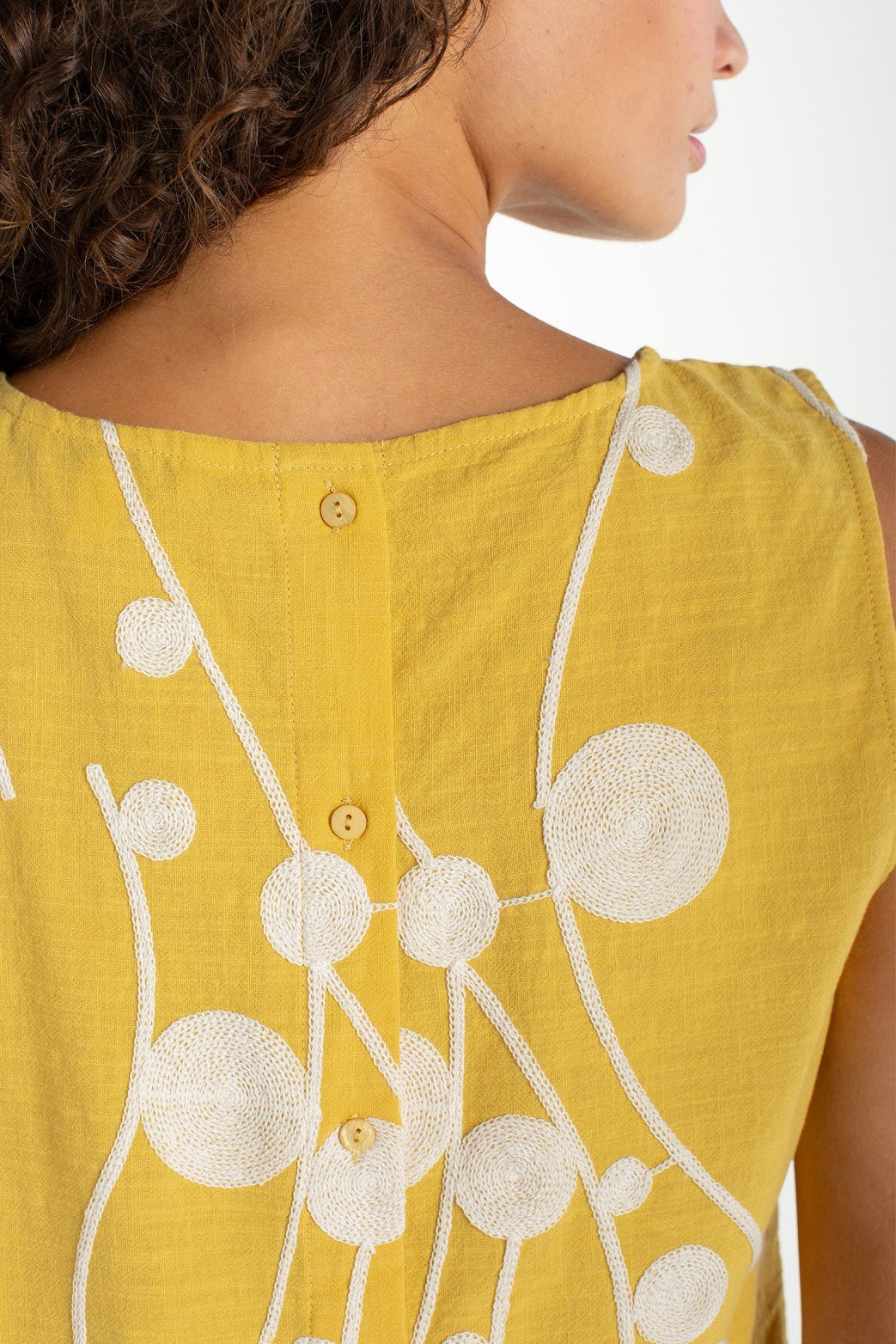 Yellow sleeveless top with cream embroidered circular botanical design and button back closure