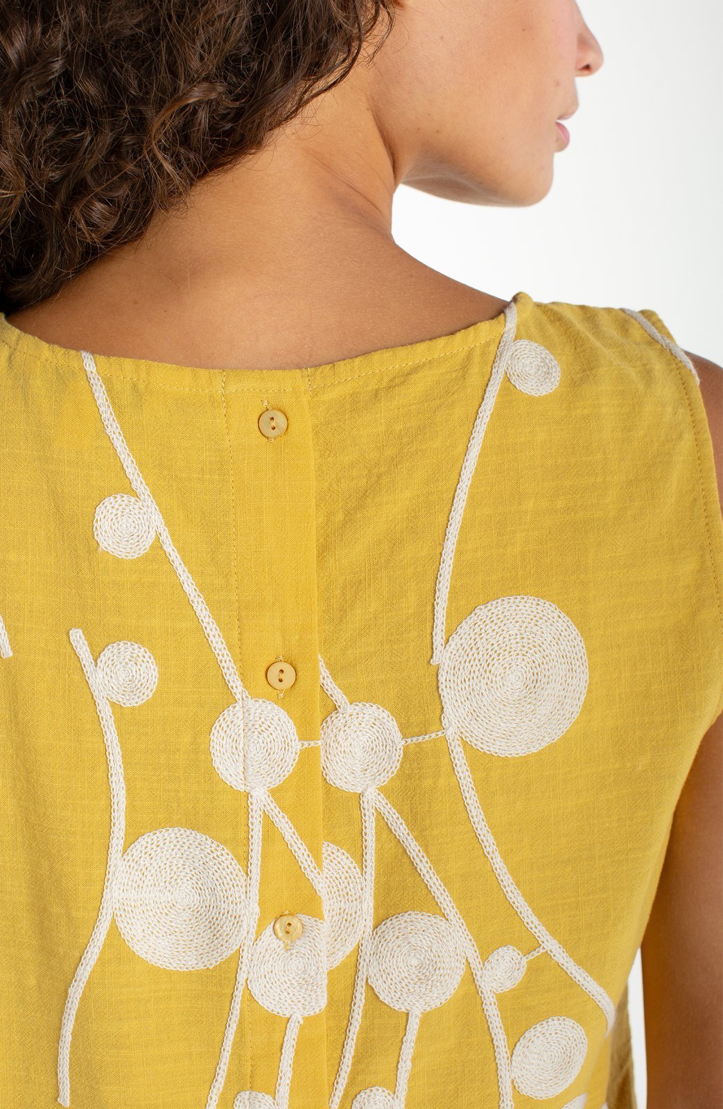 Yellow sleeveless top with cream embroidered circular botanical design and button back closure