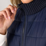 Woman zipping navy quilted sweater vest with ribbed knit turtleneck collar detail