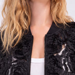 Black bomber jacket with 3D rosette appliqué detail on sheer mesh base, close-up view