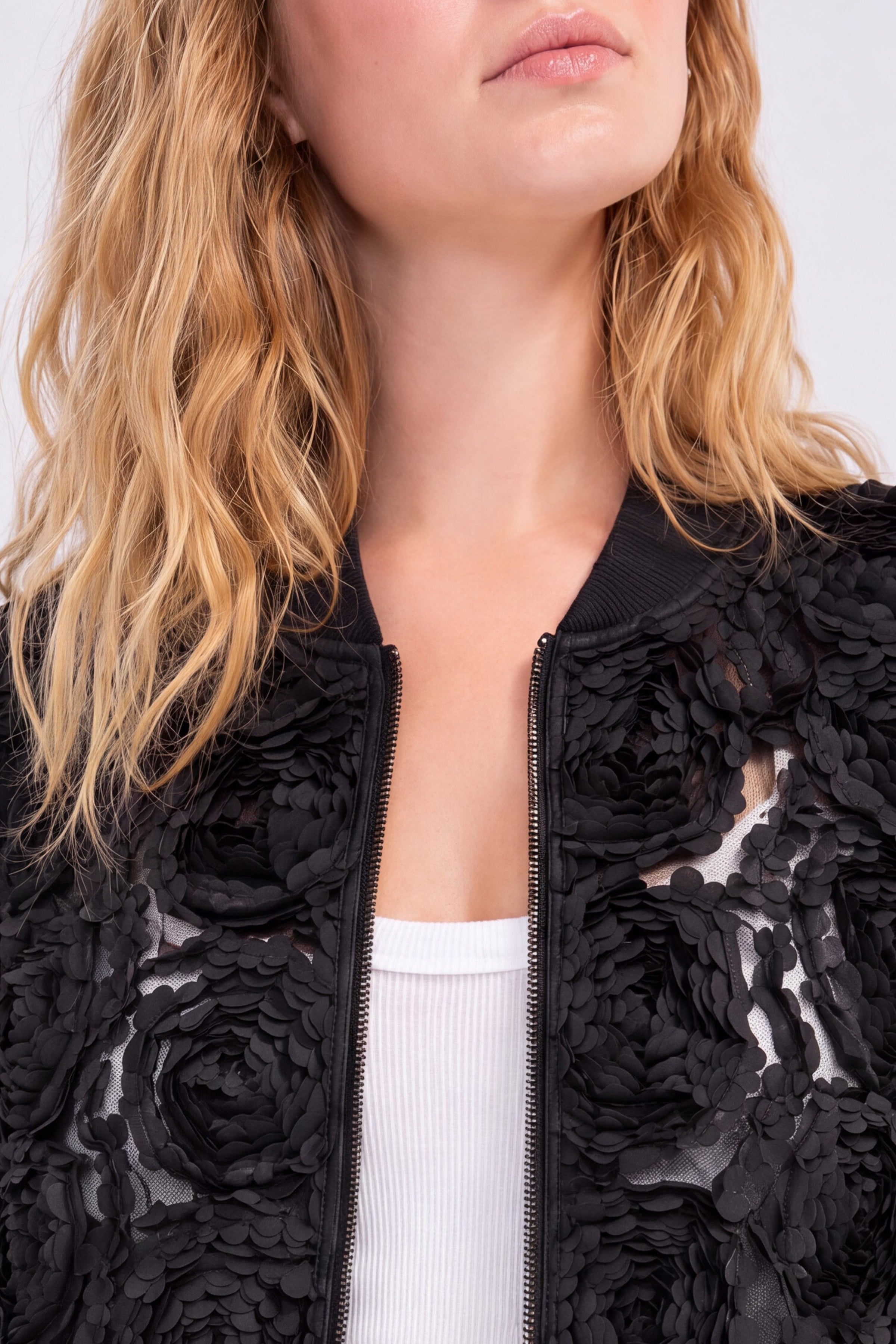 Black bomber jacket with 3D rosette appliqué detail on sheer mesh base, close-up view