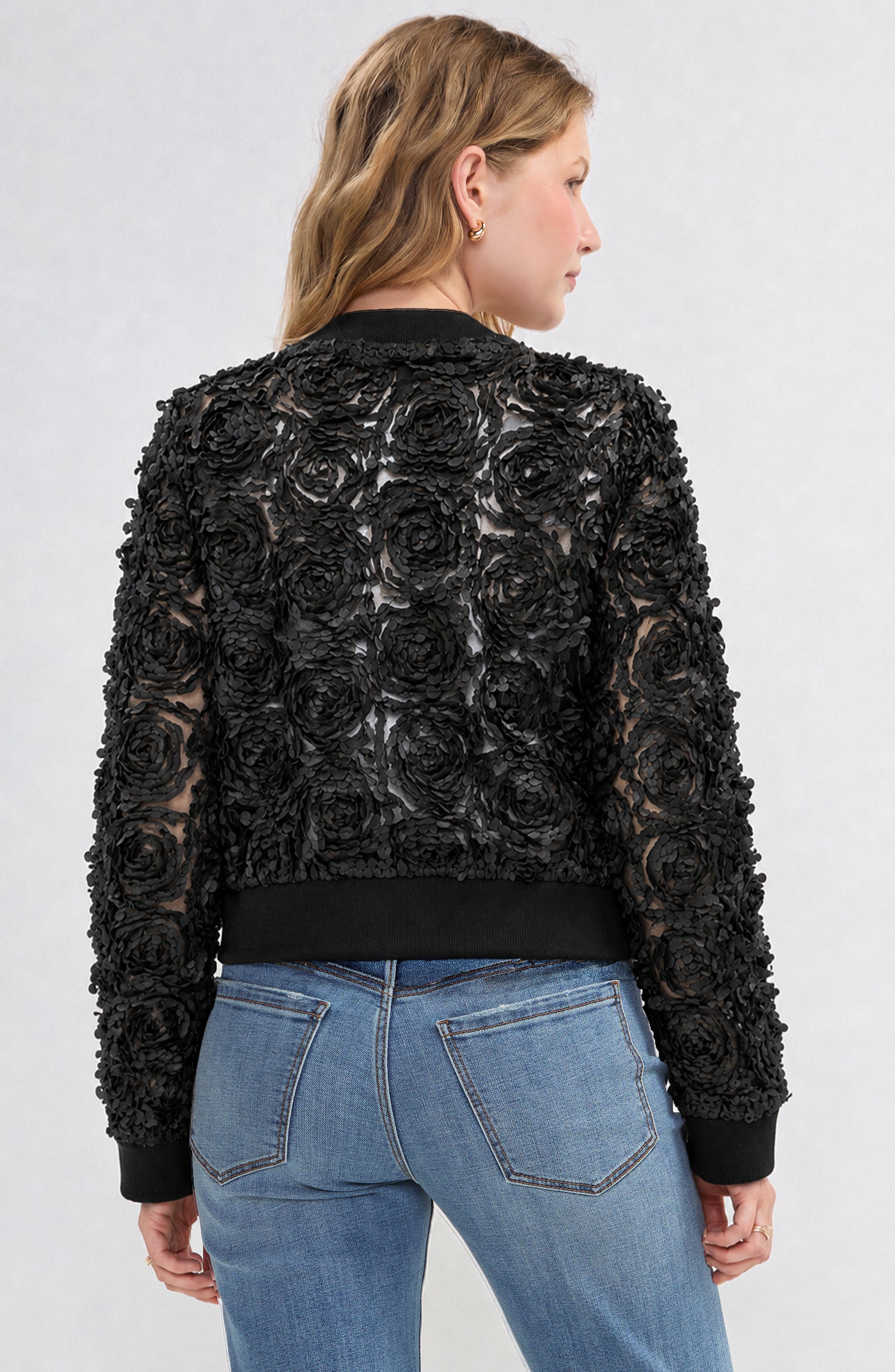 Black rosette bomber jacket with ribbed trim shown from back on female model with jeans